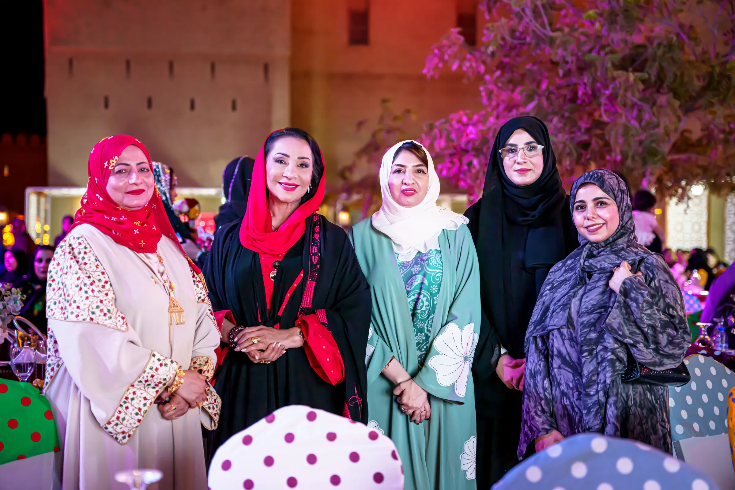 خمس نساء عُمانيات بأزياء ملونة يقفن معًا خلال أمسية في ساحة الحصن